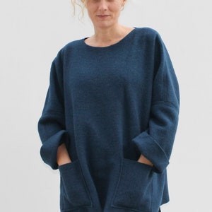 Op de afbeelding: Een oversized donkerblauwe trui met lange mouwen en twee grote opgestikte zakken. De trui heeft een losse pasvorm en een ronde hals.