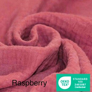 May include: Close-up of raspberry-colored fabric with soft folds and textures. The word "Raspberry" is printed in black at the bottom left. A green and white "OEKO-TEX" label is in the bottom right corner.