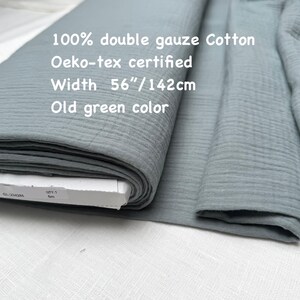 May include: A roll of old green double gauze cotton fabric. The fabric is 56 inches wide and Oeko-tex certified. The text on the image reads "100% double gauze Cotton", "Oeko-tex certified", "Width 56"/142cm", and "Old green color".