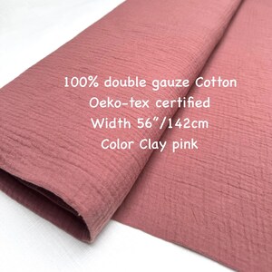May include: A folded piece of clay pink double gauze cotton fabric. The fabric is 56 inches wide and Oeko-tex certified. The text on the fabric reads: "100% double gauze Cotton, Oeko-tex certified, Width 56"/142cm, Color Clay pink."