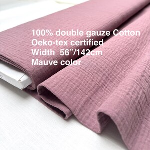 May include: Mauve-colored double gauze cotton fabric. The fabric is 56 inches wide and Oeko-tex certified. The image shows the fabric folded and rolled, highlighting its texture and color. The text on the fabric reads: 100% double gauze Cotton, Oeko-tex certified, Width 56"/142cm, Mauve color.