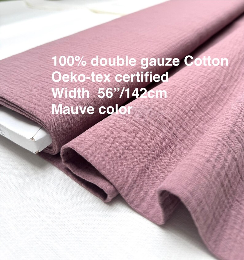 May include: Mauve-colored double gauze cotton fabric. The fabric is 56 inches wide and Oeko-tex certified. The image shows the fabric folded and rolled, highlighting its texture and color. The text on the fabric reads: 100% double gauze Cotton, Oeko-tex certified, Width 56"/142cm, Mauve color.