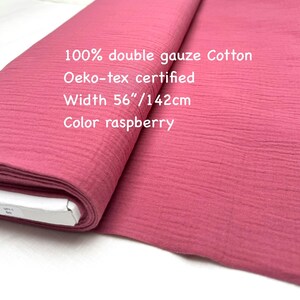May include: A roll of raspberry-colored double gauze cotton fabric. The fabric is 56 inches wide and Oeko-Tex certified. The text on the image reads "100% double gauze Cotton", "Oeko-tex certified", "Width 56"/142cm", and "Color raspberry".