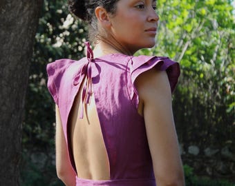 May include: A woman wearing a purple linen dress with a low back and ruffled sleeves. The dress has a tie at the back of the neck.