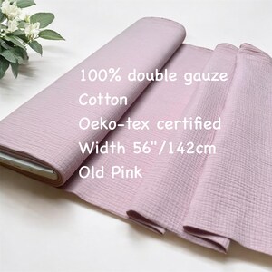 May include: Old pink 100% double gauze cotton fabric. The fabric is Oeko-tex certified and is 56 inches wide. The fabric is rolled up and partially unrolled, showing its texture. The text on the fabric reads "Old Pink".