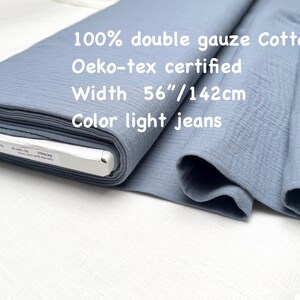 May include: A roll of light blue double gauze cotton fabric. The fabric is 56 inches wide and is Oeko-tex certified. The text on the fabric reads "100% double gauze Cotton", "Oeko-tex certified", "Width 56"/142cm", and "Color light jeans".
