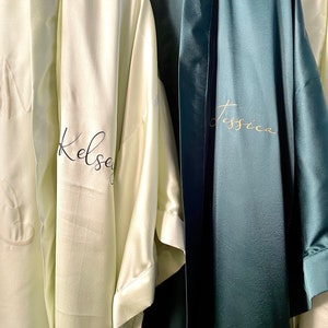 May include: Two satin robes, one light green with the name "Kelsey" embroidered in black, and the other dark green with the name "Jessica" embroidered in gold.