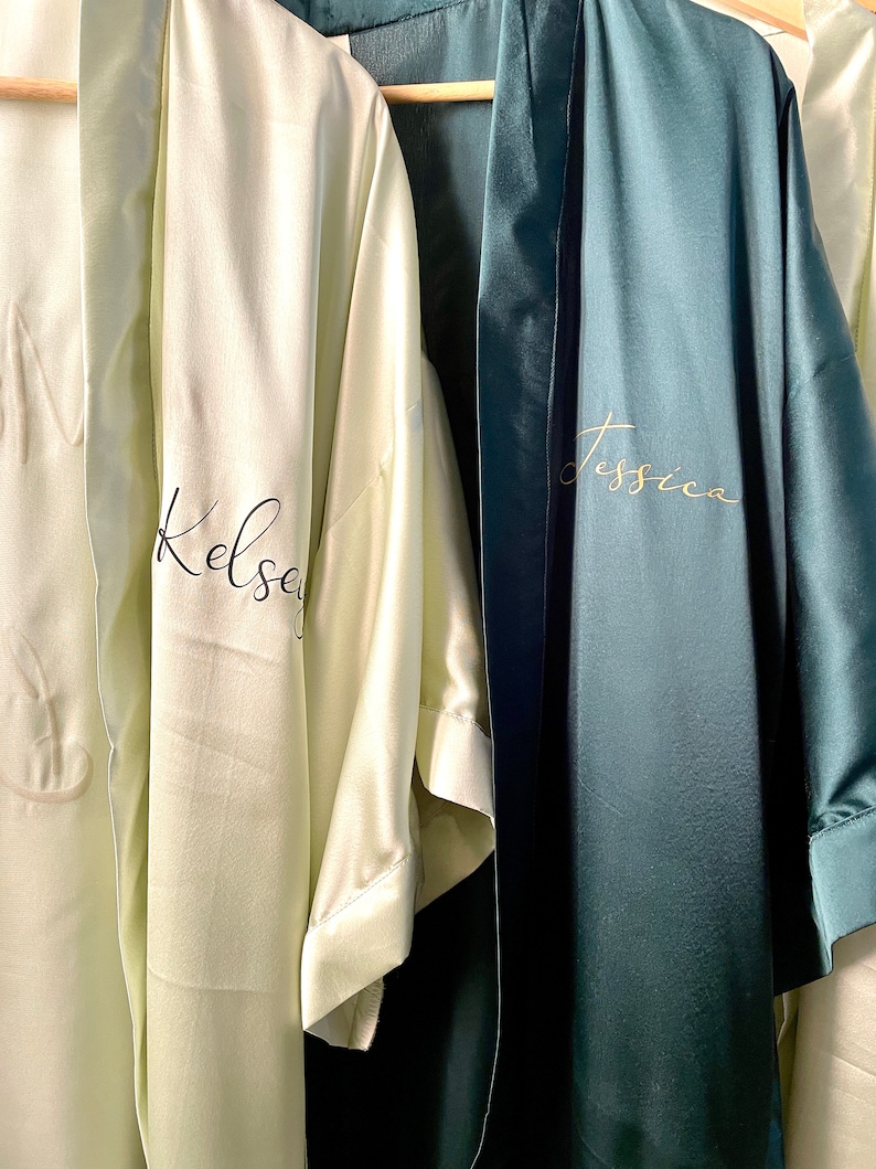 May include: Two satin robes, one light green with the name "Kelsey" embroidered in black, and the other dark green with the name "Jessica" embroidered in gold.