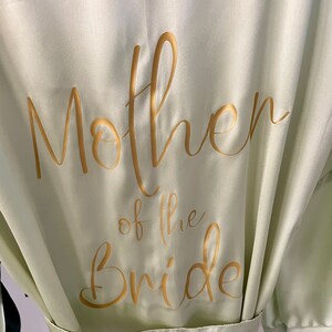 May include: A light green satin robe with gold lettering that says "Mother of the Bride".
