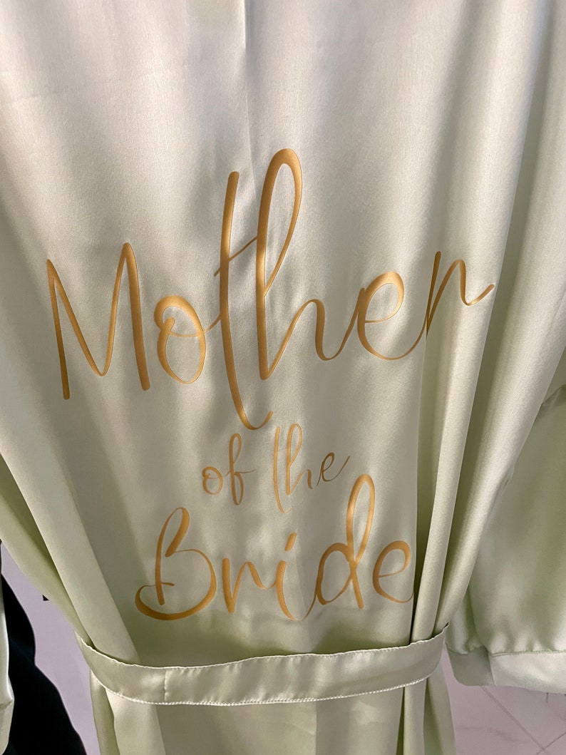 May include: A light green satin robe with gold lettering that says "Mother of the Bride".
