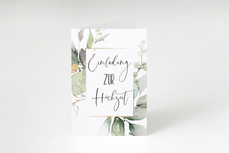 May include: A white card with a gold frame and green watercolor leaves. The text inside the frame reads "Einladung zur Hochzeit" which translates to "Invitation to the Wedding" in English.