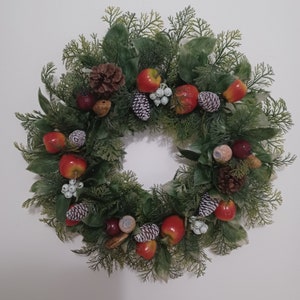 May include: A circular Christmas wreath with green foliage, red apples, pinecones, and white berries. The wreath is decorated with a variety of textures and colors, creating a festive and natural look. Perfect for holiday decor.