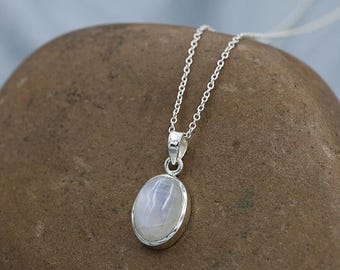 May include: A silver necklace featuring an oval-shaped moonstone pendant set in a polished silver bezel. The pendant hangs from a delicate silver chain, showcasing the smooth, translucent, and iridescent surface of the white gemstone.