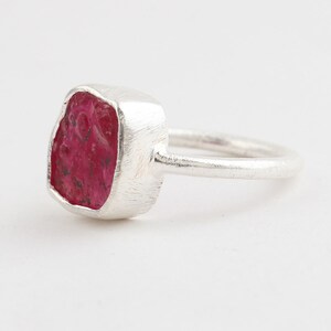 May include: A silver ring featuring a red ruby gemstone. The ruby is a rough cut and has a natural, irregular shape.