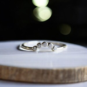 Może przedstawiać: Delikatny złoty pasek z rzędem małych okrągłych diamentów osadzonych w zakrzywionym kształcie łuku.