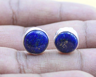 Könnte beinhalten: Ein Paar runde Ohrstecker mit polierten, tiefblauen Lapislazuli-Steinen mit natürlichen goldfarbenen Sprenkeln, die jeweils in eine einfache silberfarbene Metallfassung eingefasst sind, welche den runden Edelstein sicher hält.
