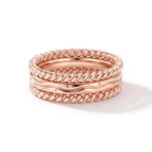 Könnte beinhalten: Ein Stapel aus drei Ringen in Roségold. Der obere und der untere Ring haben eine gedrehte Seilstruktur. Der mittlere Ring weist eine glatte, gewellte Oberfläche mit kleinen, gleichmäßig verteilten kreisförmigen Vertiefungen auf.