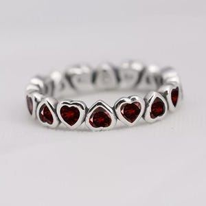May include: A silver band ring featuring a continuous row of heart-shaped settings, each containing a faceted deep red gemstone. The metal has a polished finish, and the hearts are linked together to form a complete circle around the finger.