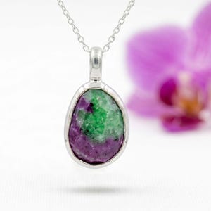 Può includere: Una collana con pendente in argento caratterizzata da una gemma di rubino zoisite a forma di goccia. La pietra presenta un mix di verde vibrante e magenta-viola intenso con una superficie naturale testurizzata, montata su una montatura in argento.