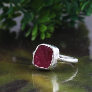 May include: A silver ring with a large, faceted, dark pink gemstone set in a square bezel.