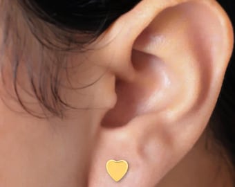 May include: A small, polished gold-tone heart-shaped stud earring secured in the earlobe. The earring features a smooth, solid surface with a rounded heart silhouette, providing a simple and clean aesthetic for everyday wear in the ear.