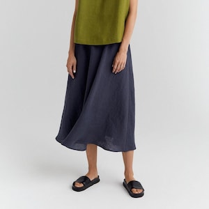 May include: A sleeveless olive green V-neck top paired with a navy blue midi skirt. The model is wearing black sandals. The outfit is made of linen and is suitable for warm weather.