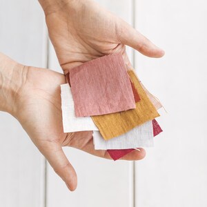 May include: A hand holding a stack of fabric swatches in various colours, including pink, white, yellow, and red.