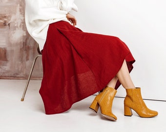 May include: A white long-sleeved mock neck sweater paired with a deep red midi-length skirt featuring a pleated design. The outfit is completed with mustard yellow ankle boots that have a textured finish and a block heel.