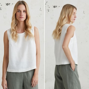 May include: A white sleeveless linen top with a scoop neck. The top is shown on a model wearing it with khaki linen trousers.