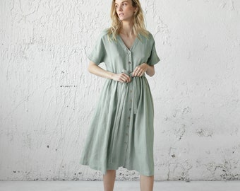 May include: A sage green linen dress with a button-up front and a tie belt. The dress has short sleeves and a v-neckline.