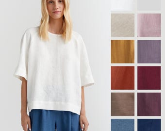 May include: A white linen top with a relaxed fit and short sleeves. The top is shown on a model with blue pants. The image also shows a variety of color swatches for the top.