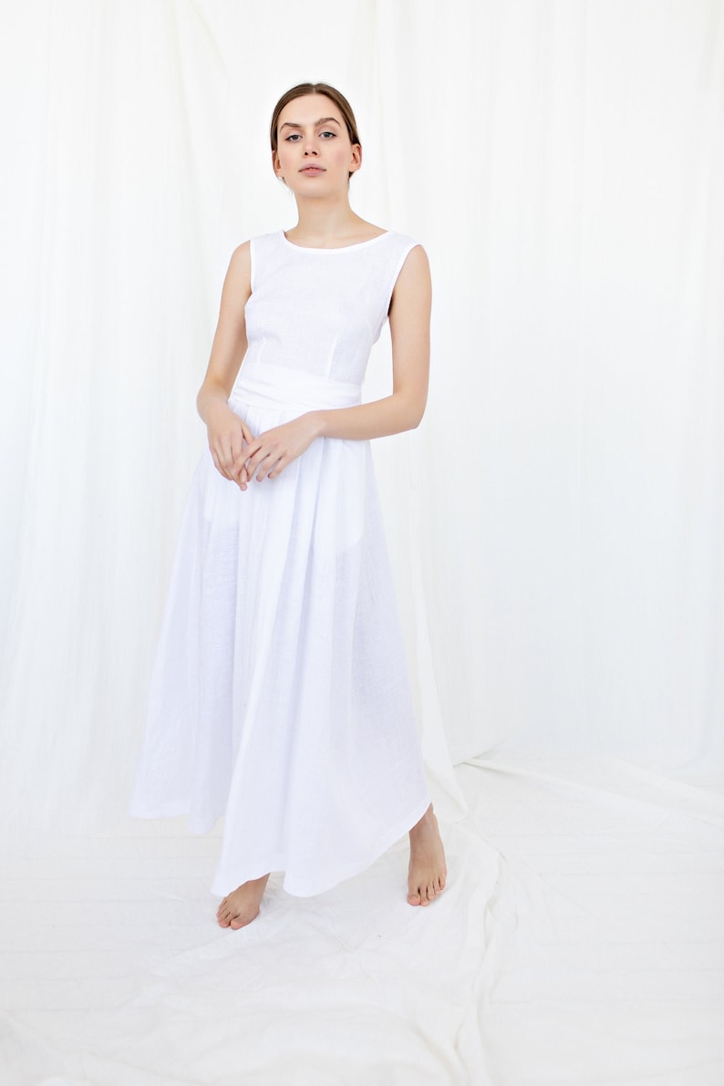 May include: A white linen dress with a sleeveless design and a fitted bodice. The dress has a flowing skirt and a simple, elegant style.