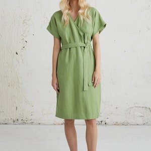 May include: A green linen wrap dress with short sleeves and a self-tie belt. The dress is knee-length and has a v-neckline.