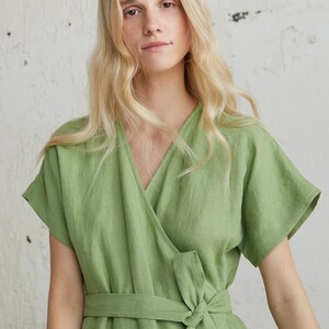 May include: A woman wearing a green linen wrap dress with short sleeves and a tie belt.