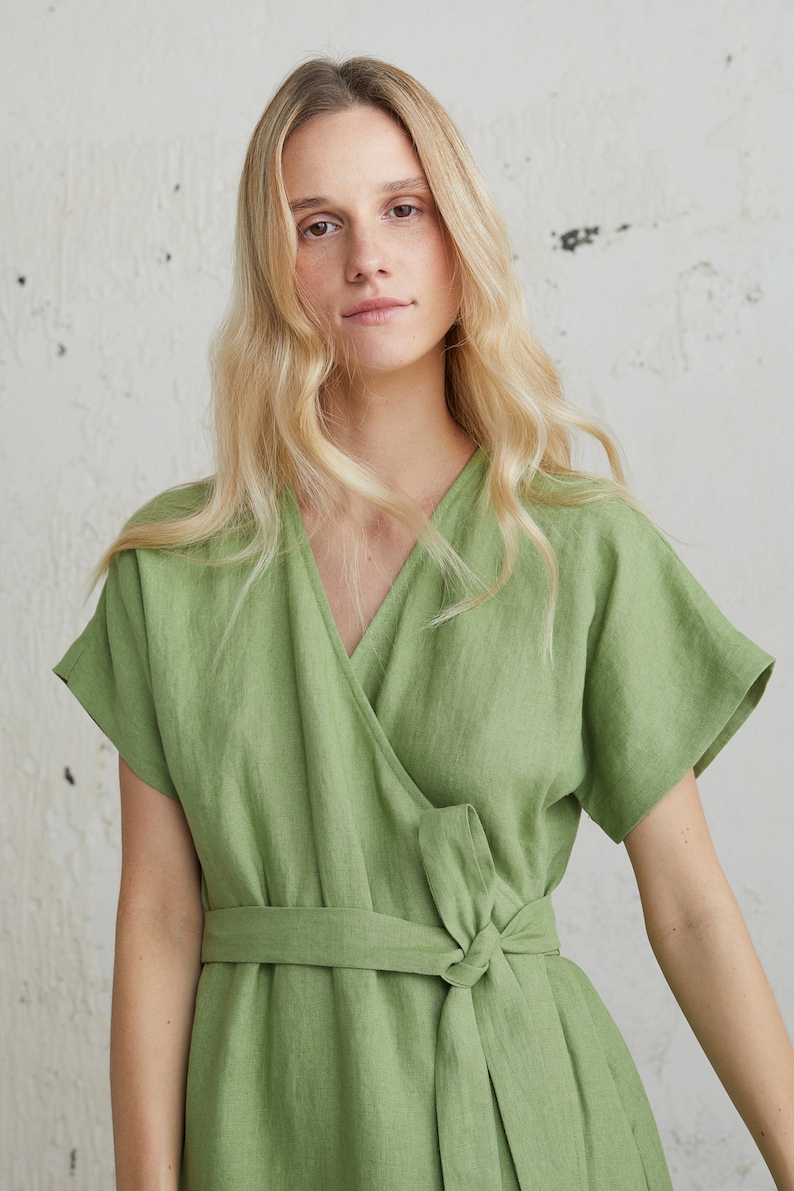 May include: A woman wearing a green linen wrap dress with short sleeves and a tie belt.