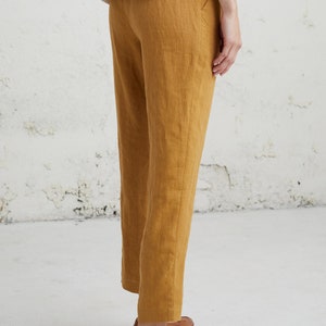 May include: A pair of mustard yellow linen pants with a straight leg fit. The pants are cropped above the ankle and have a simple, classic design.