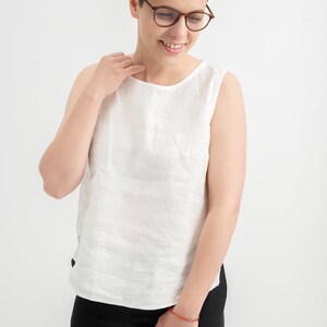 Milky White linen tank top worn with black pants, smiling model in glasses in a white studio