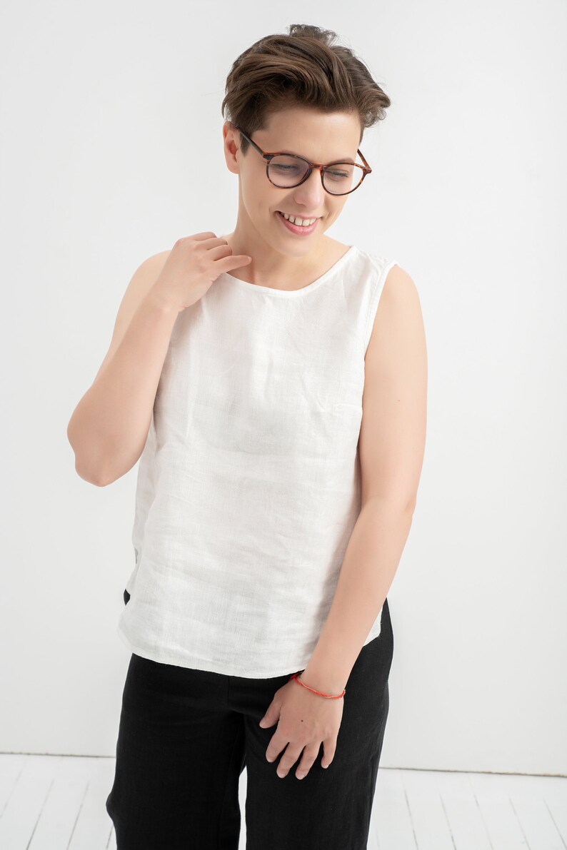 Milky White linen tank top worn with black pants, smiling model in glasses in a white studio