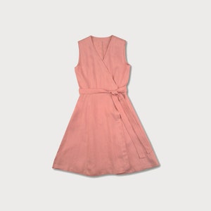 May include: A sleeveless wrap dress in a light pink color. The dress has a V-neckline and a tie belt at the waist.