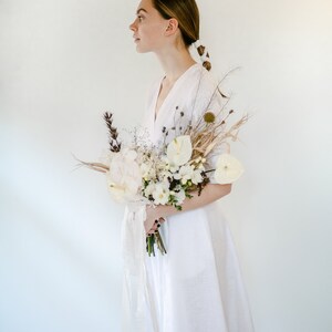 Side view of a white linen wedding dress, bride holding a bouquet