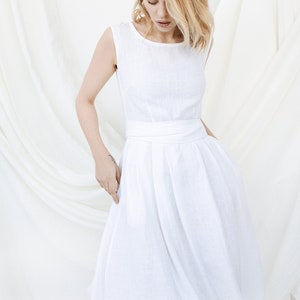 May include: A white linen dress with a sleeveless bodice and a gathered skirt. The dress has a simple, elegant design and is perfect for a summer wedding or other special occasion.
