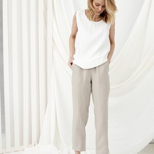 White linen tank top with Natural Linen tapered pants and green flats, model in front of draped white fabric