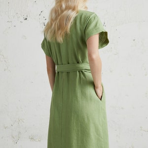 May include: A green linen dress with a short sleeve and a tie belt. The dress has a relaxed fit and a knee-length hem.