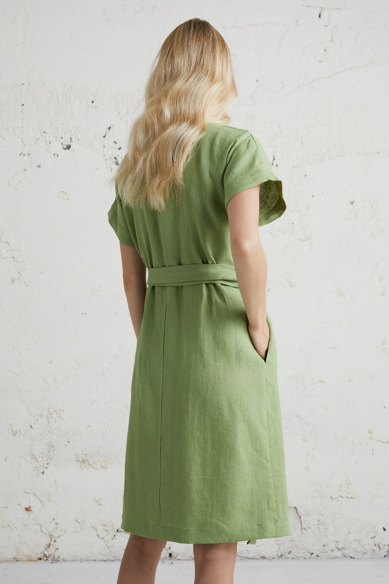 May include: A green linen dress with a short sleeve and a tie belt. The dress has a relaxed fit and a knee-length hem.