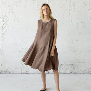 May include: A brown sleeveless linen dress with a flowing skirt. The dress is knee-length and has a simple, relaxed fit.