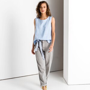 Light Blue linen tank top with a tie belt at the waist, full length studio photo with gray trousers and yellow flats