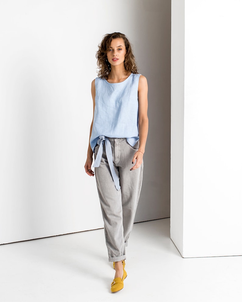 Light Blue linen tank top with a tie belt at the waist, full length studio photo with gray trousers and yellow flats