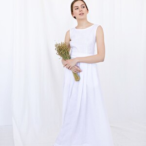 May include: A woman in a white linen dress holds a bouquet of dried flowers. The dress has a simple, sleeveless design and a flowing skirt.