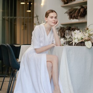 White linen wedding dress with sleeves, bride sitting at a reception table