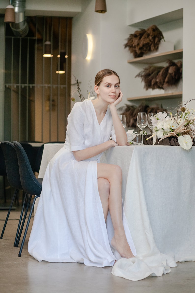 White linen wedding dress with sleeves, bride sitting at a reception table